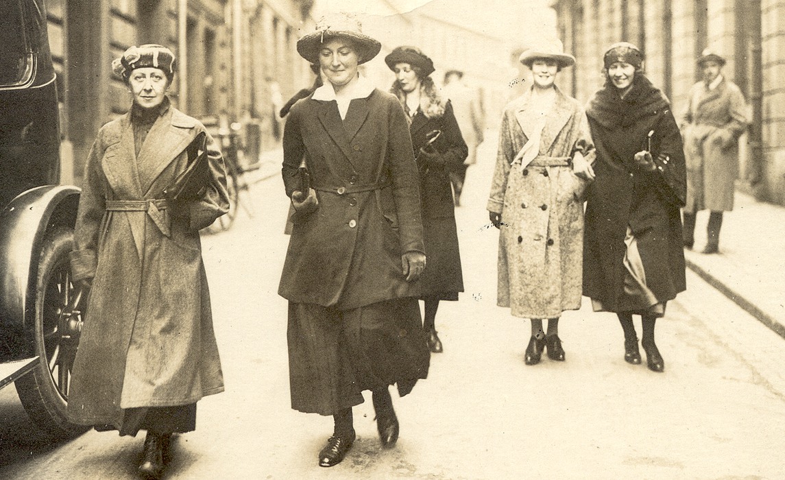 Personalen på Eva Andéns advokatbyrå går till röstning 1921. Fem kvinnor, möjligen en sjätte skymd, på en gata i Stockholm. I bakgrunden två män, till vänster del av en bil, bakom den en skylt med texten "Stadsbud". Kvinnorna bär ytterkläder, kappor eller dräkter, och hatt.