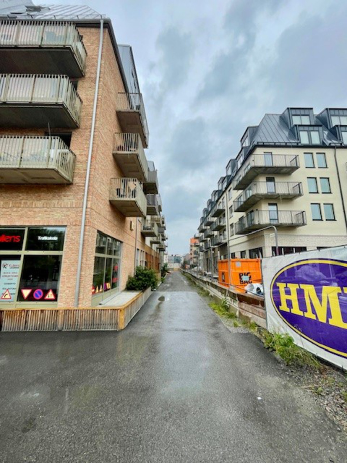 Gränd mellan två flerfamiljshus. Byggnadsställningar till höger och en trafikskola till vänster.