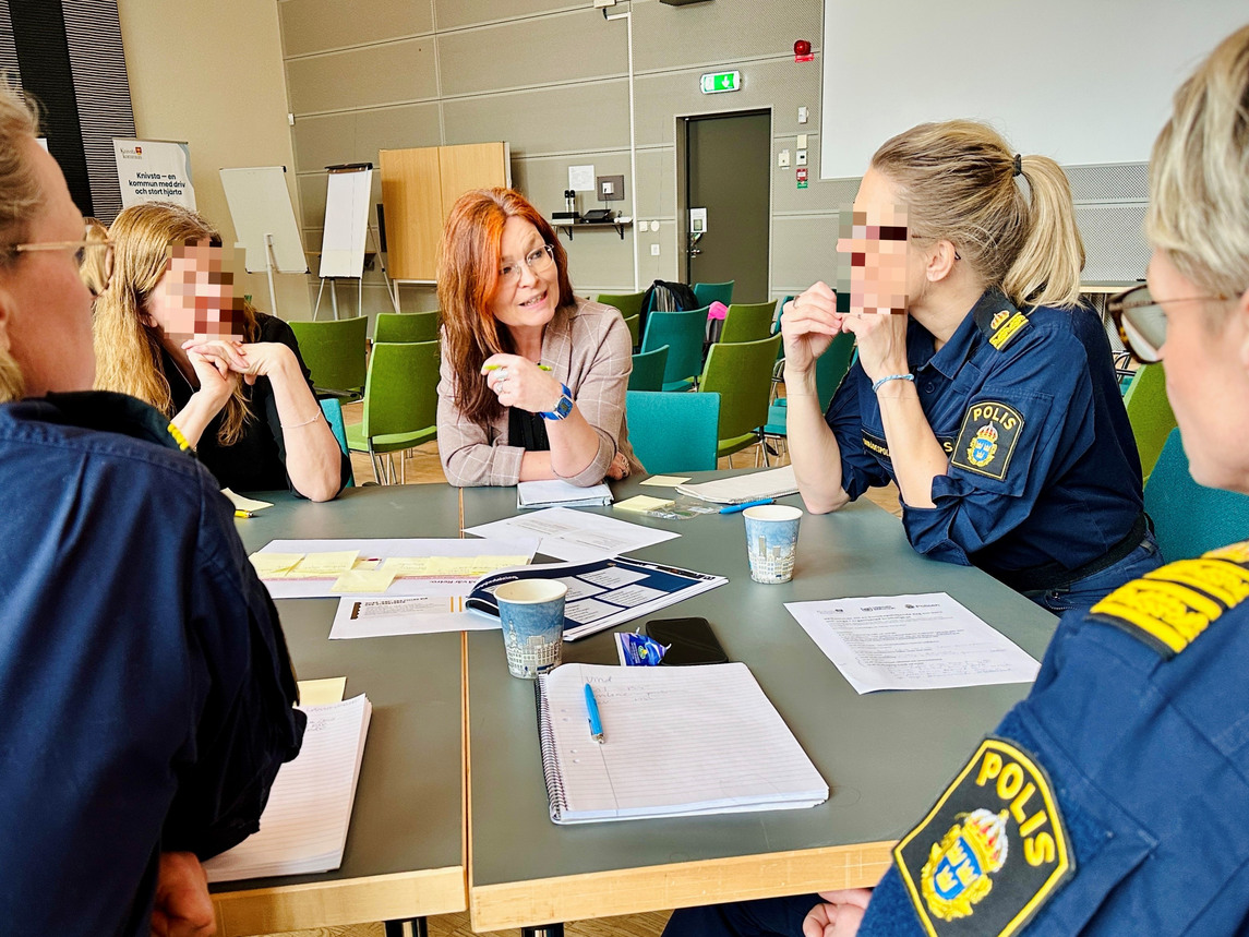 Fem kvinnor sitter och diskuterar vid ett bord - några av dem har polisuniform.