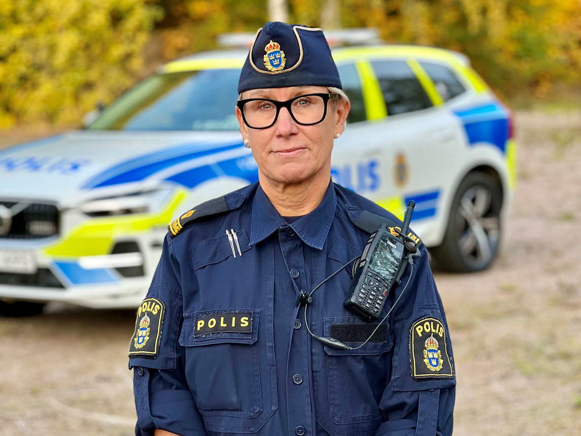 Kvinnlig polis i uniform framför en polisbil.