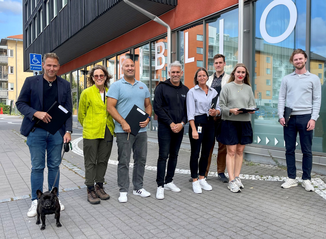 Åtta personer står framför kommunhuset med block och pennor. Mannen längst till vänster har en svart fransk bulldog i koppel.