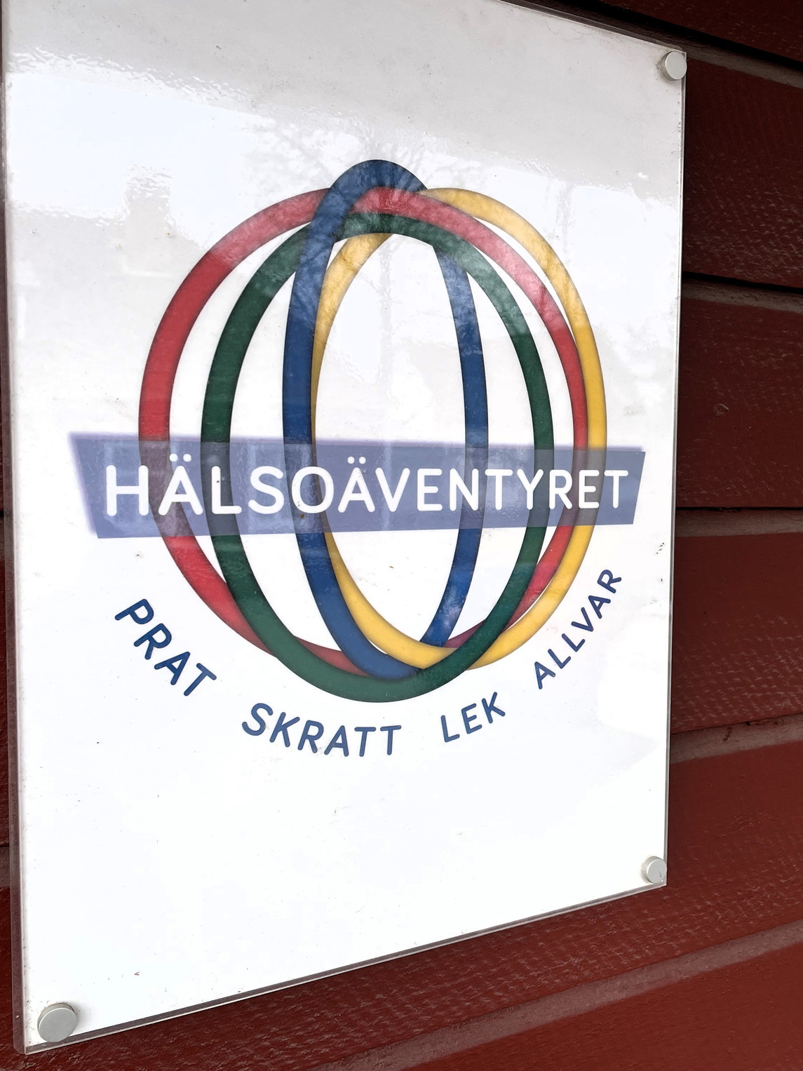 En skylt på en röd fasad med texten: Hälsoäventyret prat skratt lek allvar