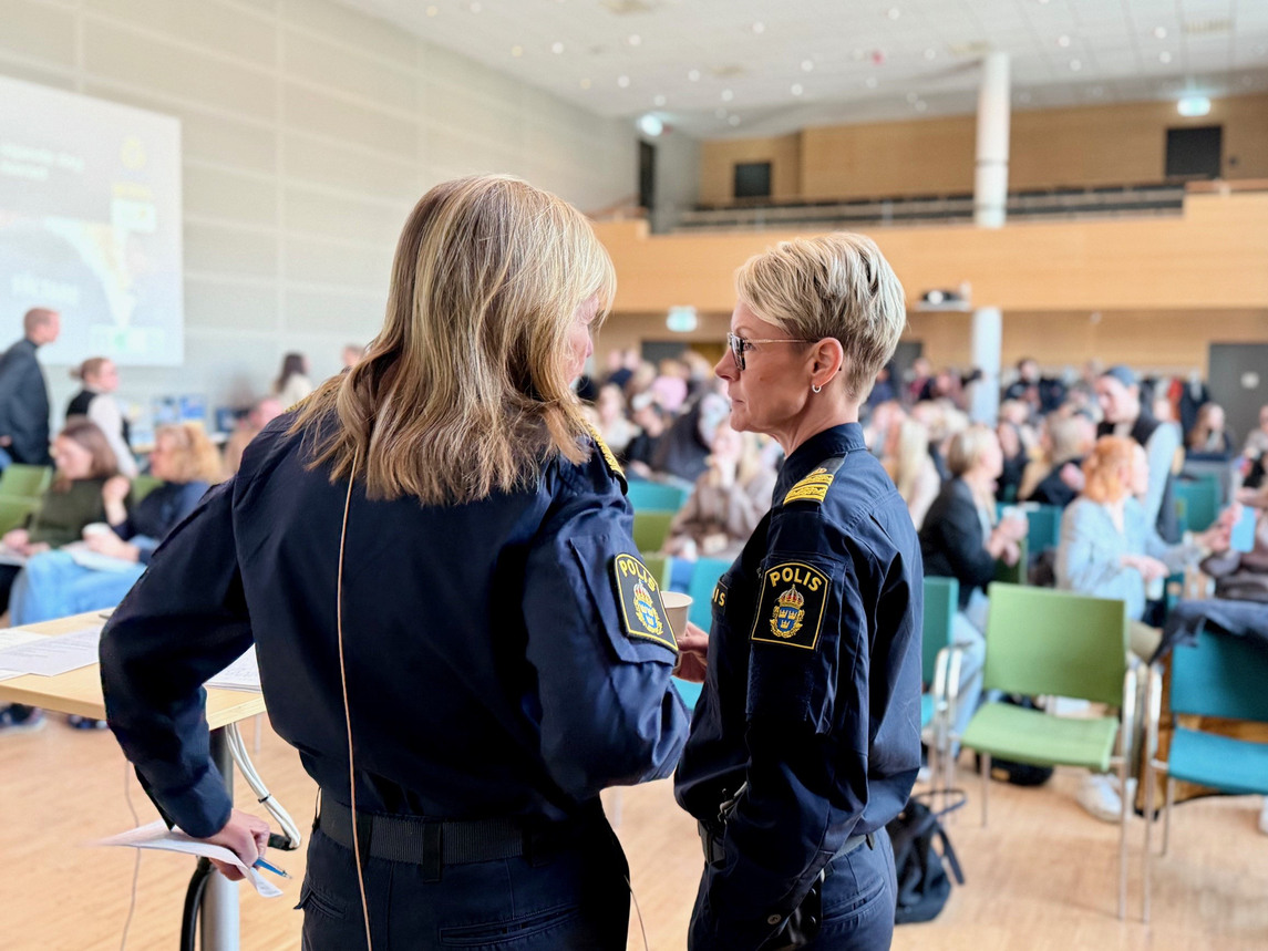 Två kvinnliga poliser står och pratar i en sal, i bakgrunden många människor.