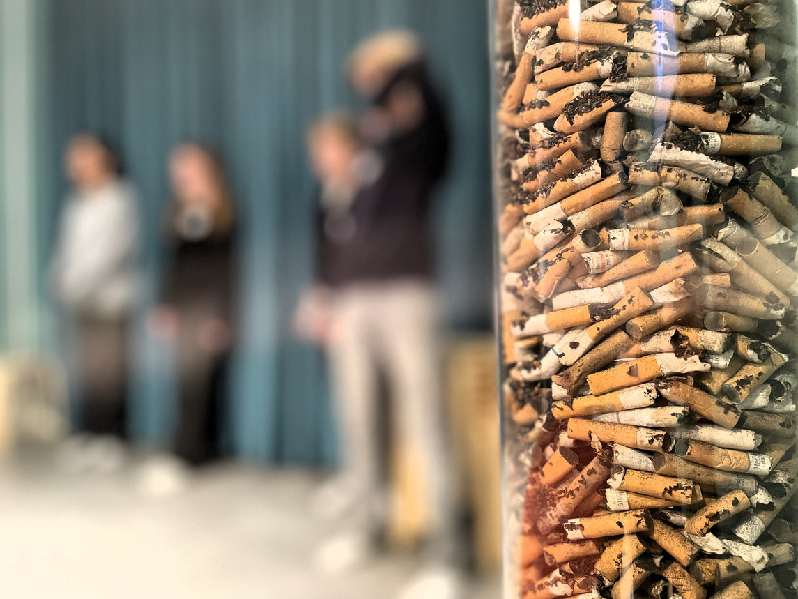 Cigarettfimpar i ett plaströr - tre ungdomar i bakgrunden.