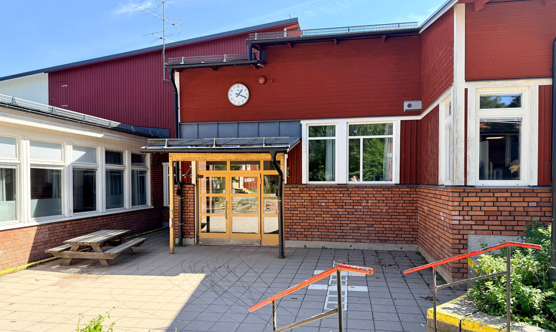Skolbyggnad med röd träpanel, tegel samt en gul dörr.