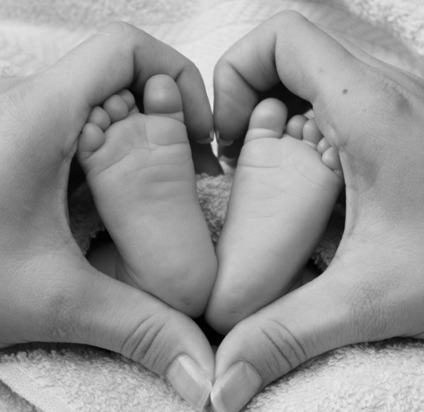 bebisfötter som hålls om av vusenhänder, formar hjärta om bebisfötterna